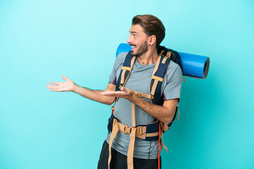 Young mountaineer man with a big backpack isolated on blue background with surprise facial...