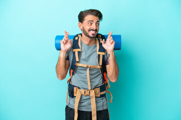 Young mountaineer man with a big backpack isolated on blue background with fingers crossing