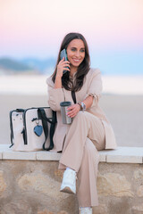 Happy beautiful businesswoman talking on the phone on the shore at sunset