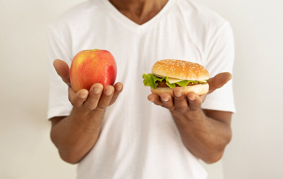 Black man weighing options between burger and apple at kitchen