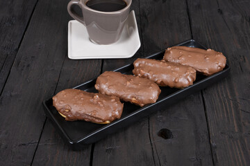 Chocolate eclair cakes on wooden background. Coffee cup next to it.