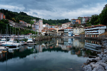 Fototapeta na wymiar View of Mutriku village and its reflection in the harbor waters in the morning under a dramatic cloudy sky, Gipuzkoa, Basque Country, Spain