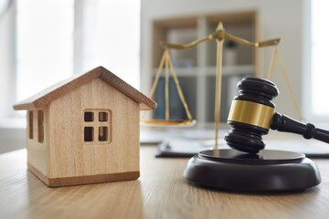 Closeup wooden toy house and close up judge's gavel on table with scales of justice in courtroom or...