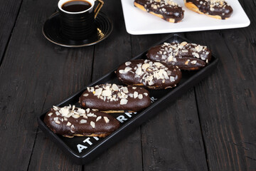 Chocolate eclair cakes on wooden background. Coffee cup next to it.