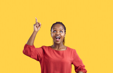 Excited joyful dark-skinned woman points her finger at copy space isolated on yellow background....