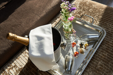 Tray with a bottle of champagne in a champagne bucket with ice, chocolates and two glasses of champagne on the bed with a bouquet of roses