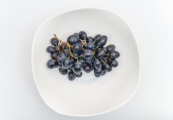 Bunches of blue grapes in white plate on white background. Berries, summer harvest, healthy eating