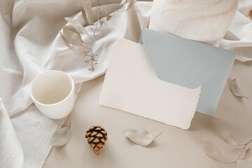 Empty white paper mockup, envelope, linen cloth, modern ceramics, twigs, cones. Marketing, wedding, holiday concept.