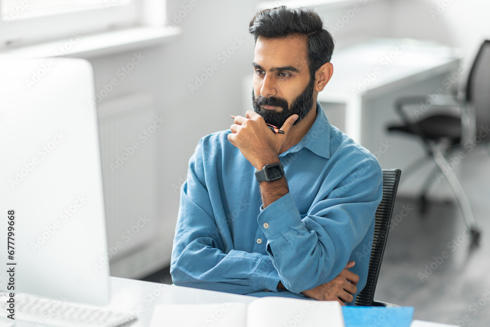 Poster thoughtful indian man with beard looking at computer