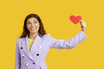 Funny girl in fashionable suit looking at red Valentine heart, studio shot. Pretty woman receives...