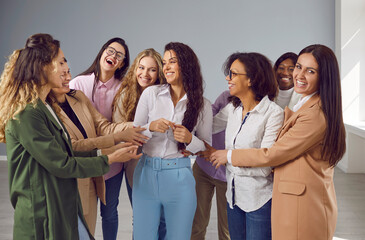 Team of happy business women congratulating their friend on her success and having fun together. Group of cheerful, diverse, mixed race ladies hug a joyful young woman during a meeting in the office