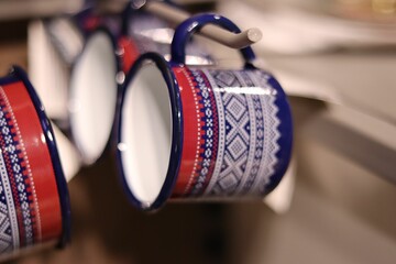 Selective focus of colorful enameled mugs hanging on holders - obrazy, fototapety, plakaty