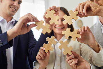 Portrait of a happy smiling group of business people assembling wooden puzzle in office. Company...