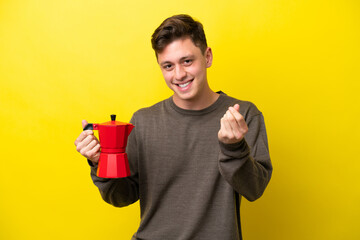 Young Brazilian man holding coffee pot isolated on yellow background making money gesture