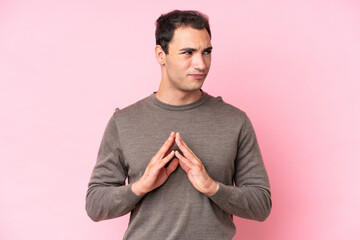 Young caucasian man isolated on pink background scheming something