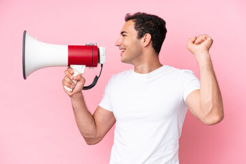 Young caucasian man isolated on pink background shouting through a megaphone to announce something...