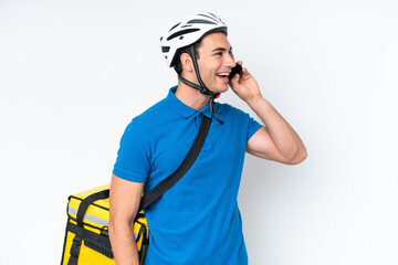 Young caucasian man with thermal backpack isolated on white background keeping a conversation with the mobile phone