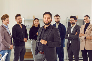 Smiling, happy businessmen stand around their colleague and greet new team member at work. Portrait of handsome, young man in business suit against the background of his business partners.