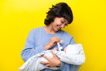 Young Argentinian woman with her cute baby isolated on yellow background