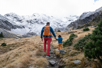 Back view of a father and his little daughter hiking in mountains during a winter day.