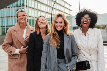 Group of proud businesswomen smiling and looking at camera at workplace. Real executive women staring front, laughing together with suit and successful expression. Corporate female employees meeting - obrazy, fototapety, plakaty
