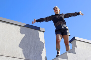 Eine junge Frau steht mit offenen Armen hoch oben auf einer Treppe