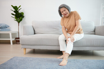 senior woman suffering from knee ache on sofa