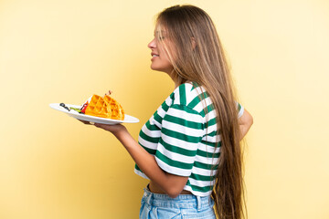 Young caucasian woman holding waffles isolated on yellow background suffering from backache for...
