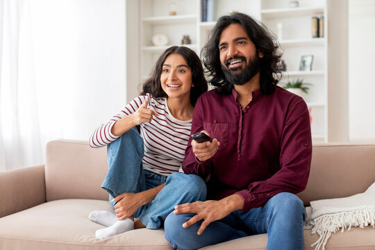 Positive young indian couple watching TV at home