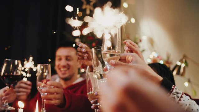 Friends Celebrating New Year, Sitting At Dining Table. International Young People Clinking Glasses With Champagne And Drinking, Toasting. Diverse Students During Christmas Party At Home. 