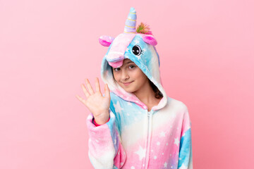 Little caucasian woman wearing a unicorn pajama isolated on pink background saluting with hand with...