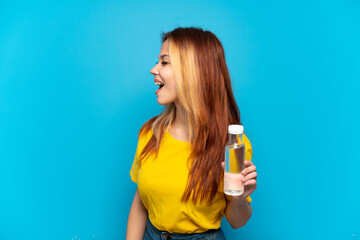 Teenager girl with a bottle of water over isolated blue background laughing in lateral position