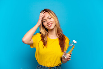 Teenager girl with a bottle of water over isolated blue background smiling a lot