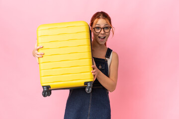 Teenager Russian girl isolated on pink background in vacation with travel suitcase and surprised