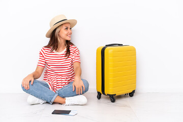 Young traveler girl sitting one the floor isolated on white background in lateral position