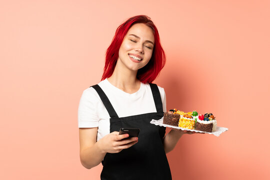 Pastry chef holding a muffins isolated on pink background with phone in victory position