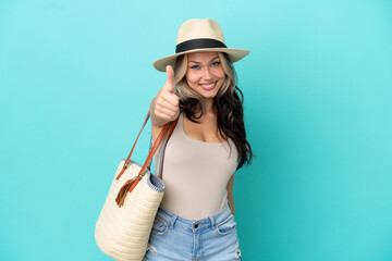 Fototapeta premium Teenager Russian girl with pamel and beach bag isolated on blue background with thumbs up because something good has happened