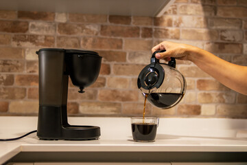 A woman's hand pours coffee from a coffee pot into a cup in the kitchen. Family life. 