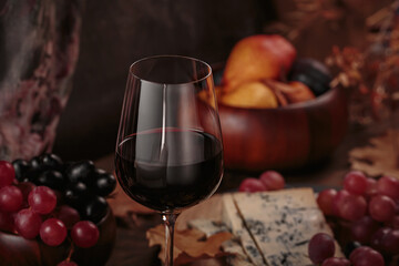 Glass of red wine served with blue cheese on dark wooden background. Autumn picnic with wine and cheese platter, fruits and dry leaves in rustic style