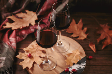 Autumn still life with two glasses of red wine and dry leaves in rustic style on dark wooden background. Romantic sweater weather concept