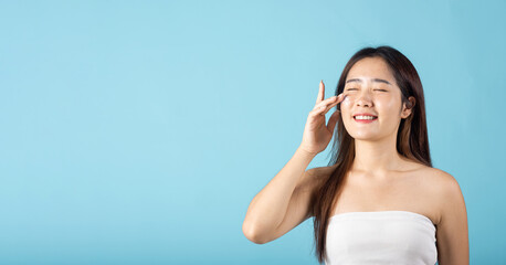 Happy beauty portrait woman gets cream on her cheek, Beautiful young female smiling applying cosmetic cream on her face isolated on blue background, health clean skin, Skin care and beauty concept