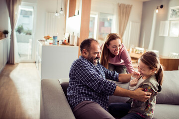 Happy family with little daughter playing at home on couch
