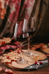 Autumn cozy still life with two glasses of red wine, book and dry leaves in rustic style on dark wooden background. Wine tasting, sweater weather concept