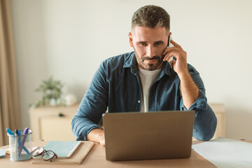 businessman answering calls on mobile phone while using laptop indoor