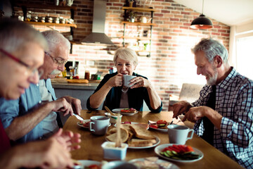 Senior people sitting at dining table together having breakfast - obrazy, fototapety, plakaty