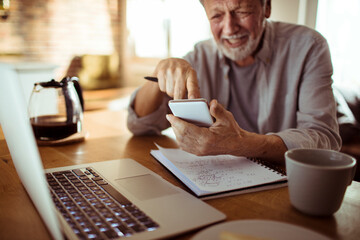 Joyful senior man using a smartphone while working at home