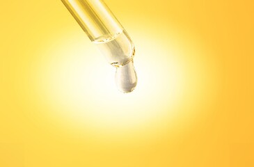 Glass lab dropper with yellow liquid on background, skincare serum