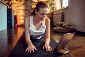 Young woman practicing yoga at home and looking at tablet for instructions