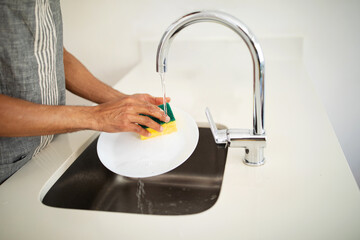 Unrecognizable African American man in apron rinses plates at kitchen