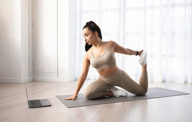 Obraz premium Athletic young woman doing yoga at home, watching fitness video